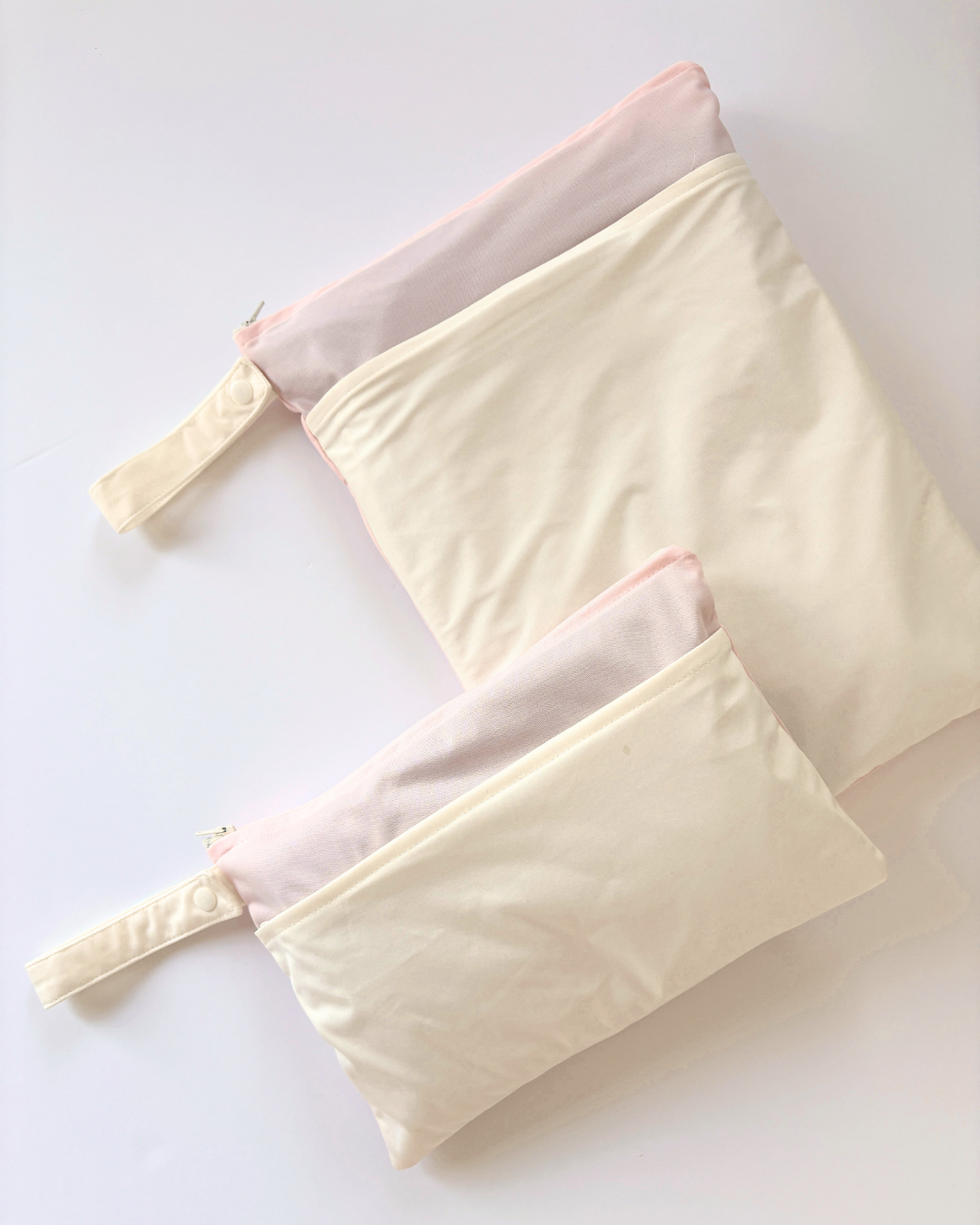 Two cream-colored waterproof wet bags with snap-closure handles and two zippered compartments, arranged diagonally on a clean white background.