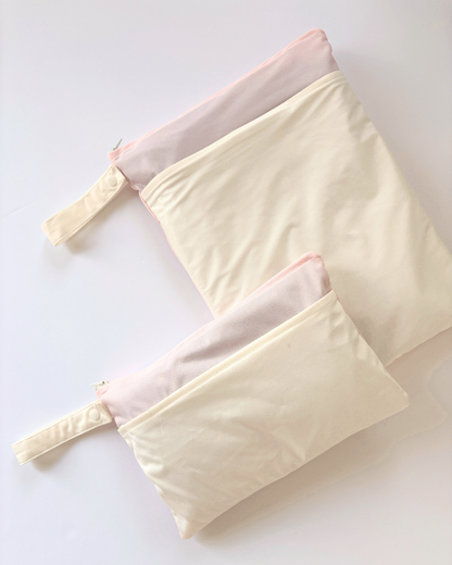 Two cream-colored waterproof wet bags with snap-closure handles and two zippered compartments, arranged diagonally on a clean white background.