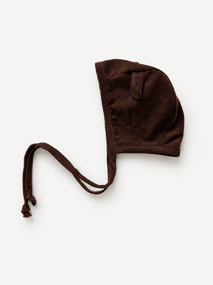 A dark brown corduroy bonnet with adjustable drawstrings, photographed flat on a light off-white background.