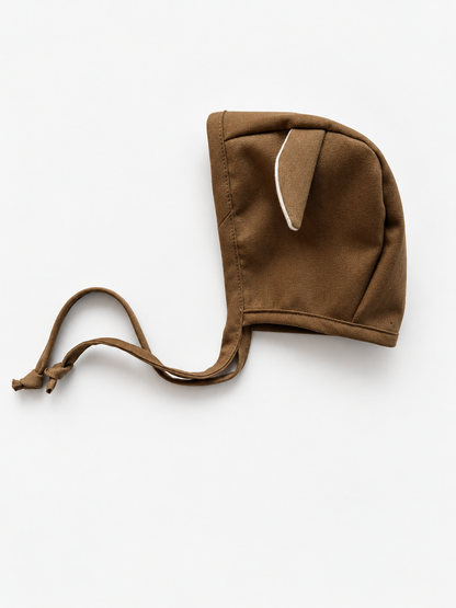 A brown fabric bonnet with a small pointed ear detail and a drawstring closure, photographed on a clean white background.