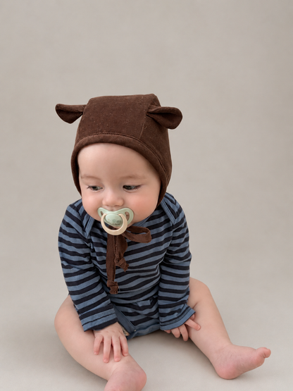 a baby wearing a brown bear baby animal bonnet sitting on a cream background