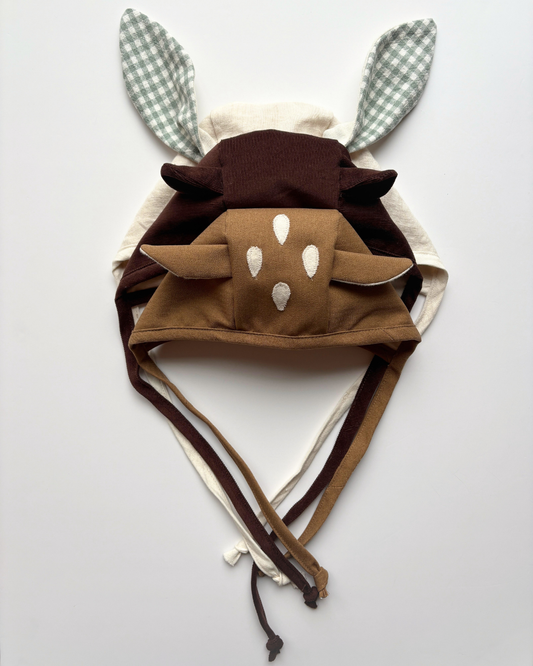 Three handmade animal baby bonnets featuring bunny, bear, and fawn designs in neutral brown, cream, and sage green fabrics. From mimi sewing company