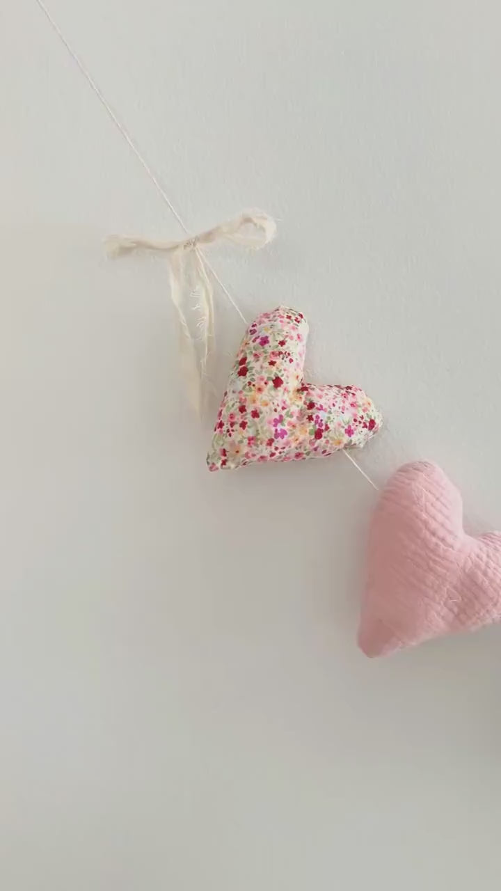 A video showing a garland of handmade fabric heart in various patterns and colors, including pink, green gingham, cream, and floral prints, arranged on a white background.