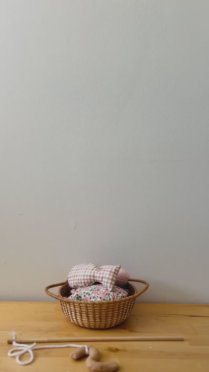 A hand holding a wooden fishing rod with a worm attached to the end, catching colorful fabric fish in a wicker basket.