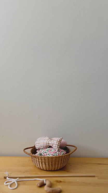 A hand holding a wooden fishing rod with a worm attached to the end, catching colorful fabric fish in a wicker basket.